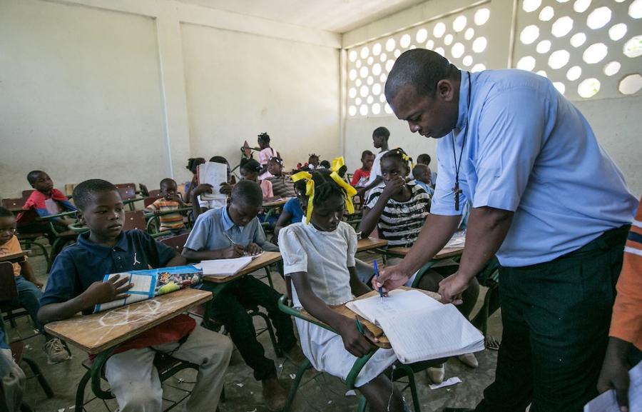 Teacher Alfred Cherfily reviews math homework by migrant children at the Notre Dame de Lourdes School in Anse-a-Pitres, Haiti.