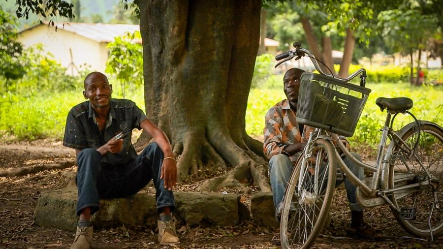 Two men rest under a group of trees that's home to hundreds of fruit bats in the town of Kilombero. The trees are a favorite shaded spot for people traveling the hot and busy stretch of road along Tanzania's Kilombero Valley, leading to concerns about inf