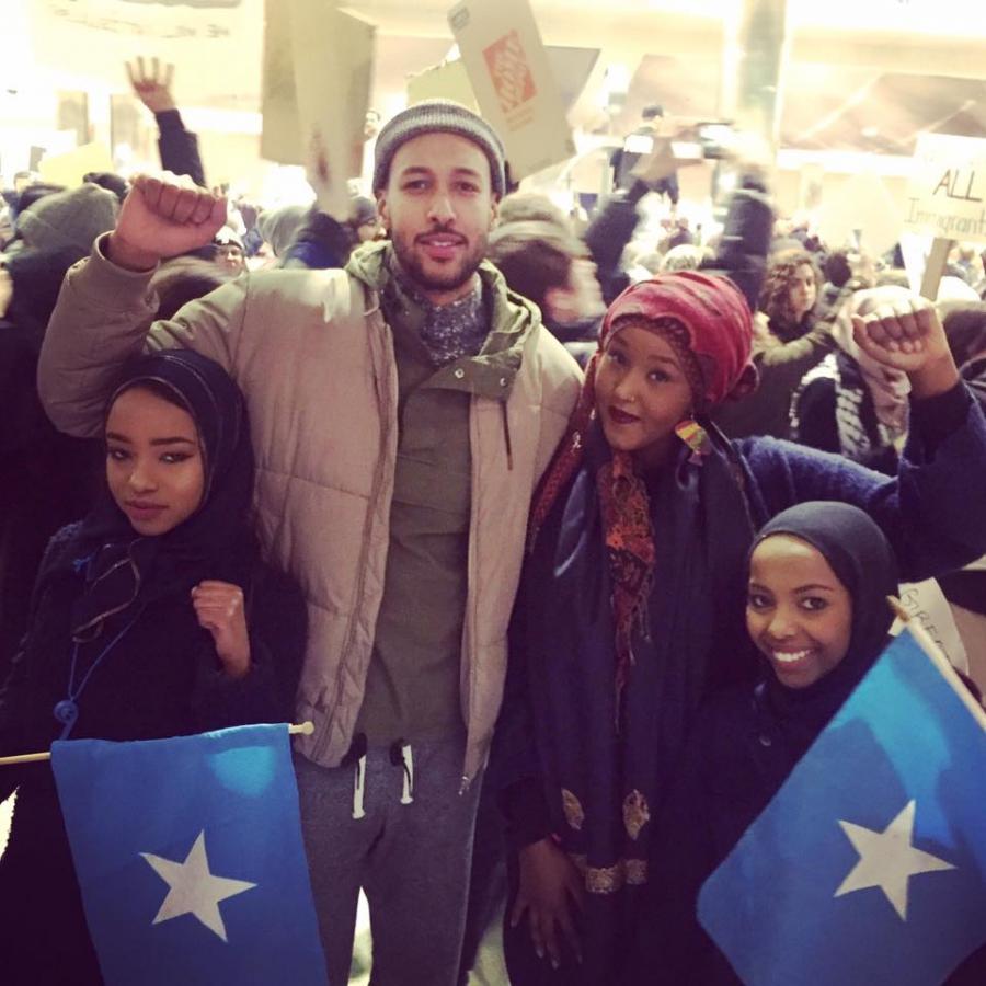 Group poses in front of protest, holding Somalia flags