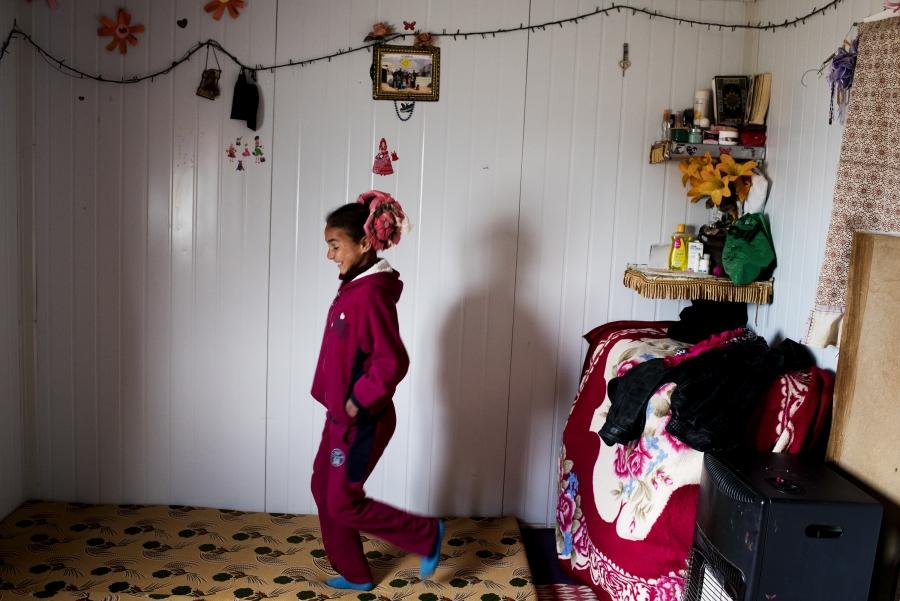 Solana, 11, walks through one of the rooms inside the family's Zaatari shelter. Behind her, a portrait of the whole family hangs among lights and decorations.