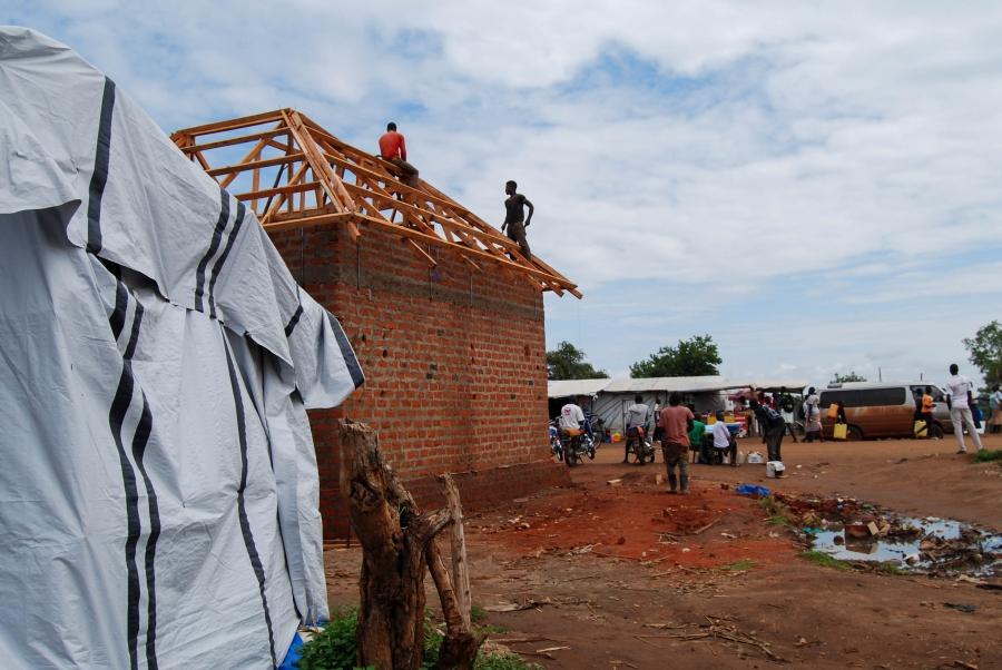 Men build a brick shop near the entrace of Bidi Bidi. Most of the buildings are temporary, but slowly permanent structures are rising up.