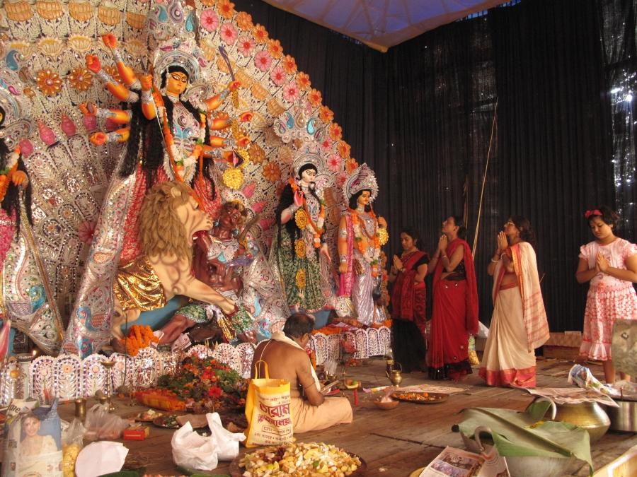 Worshippers pray to Durga with the help of a priest doing a worship ritual with chants and offerings.