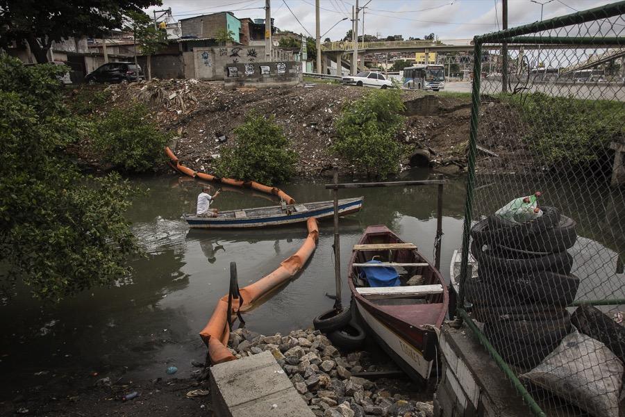 A fisherman rows through an eco-barrier that has been sliced in half on the Vila Maruí canal in the community of São Gonçalo in Rio de Janeiro.