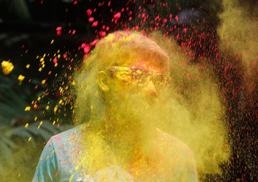 A boy stands as others throw colored powder on him during Holi celebrations.