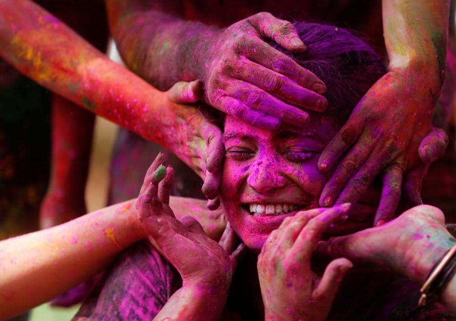 A girl reacts as others apply colored powder on her face during Holi.