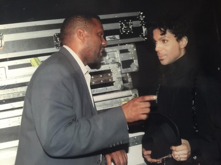 Tavis gestures to Prince in front of large carrying cases for the tour