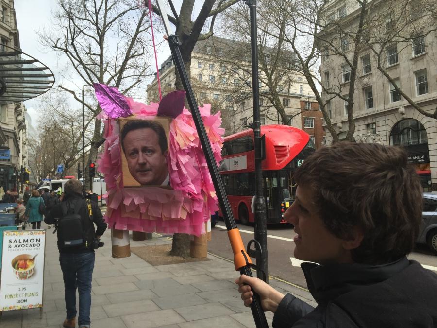 A protester carries a giant pink pig piñata with the face of Prime Minister David Cameron on its head. 