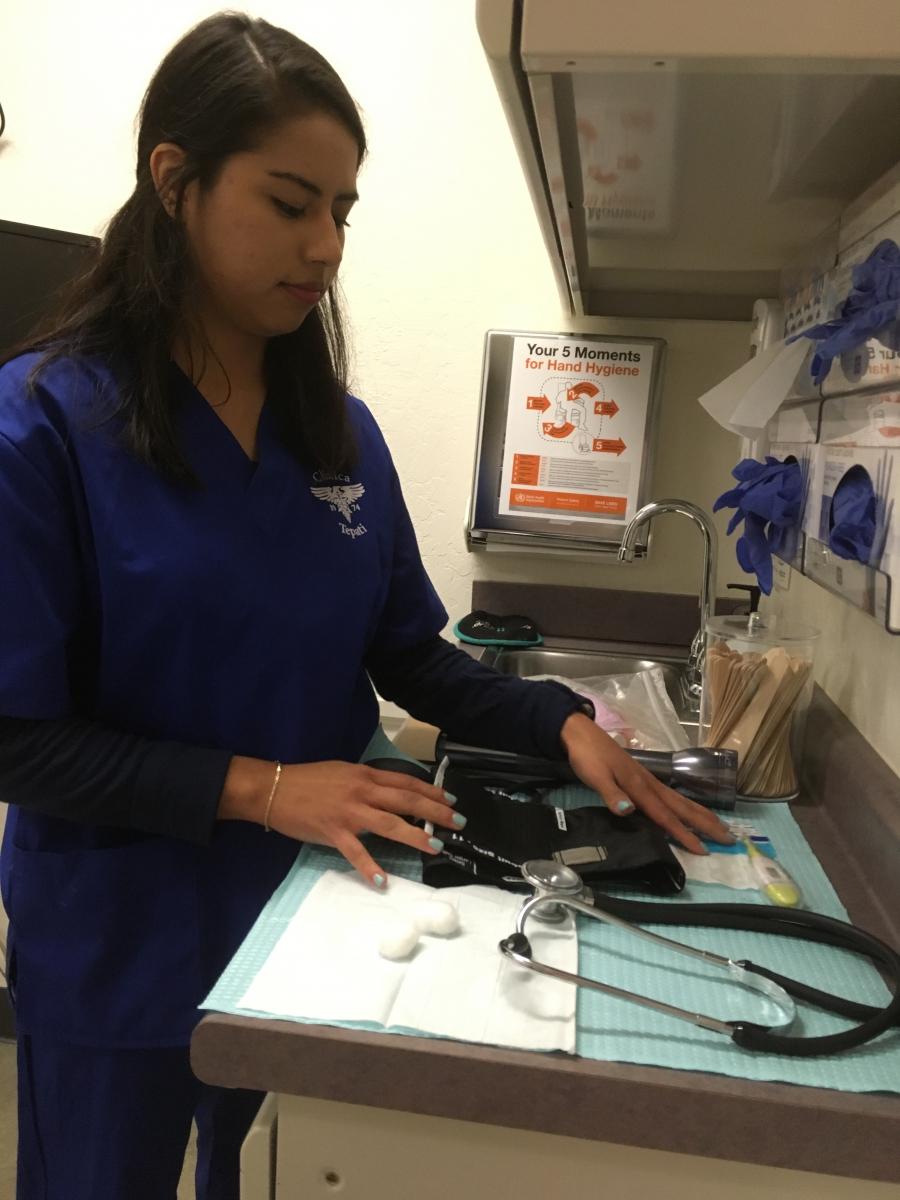 Woman in blue scrubs, standing over counter with medical tools, looking down