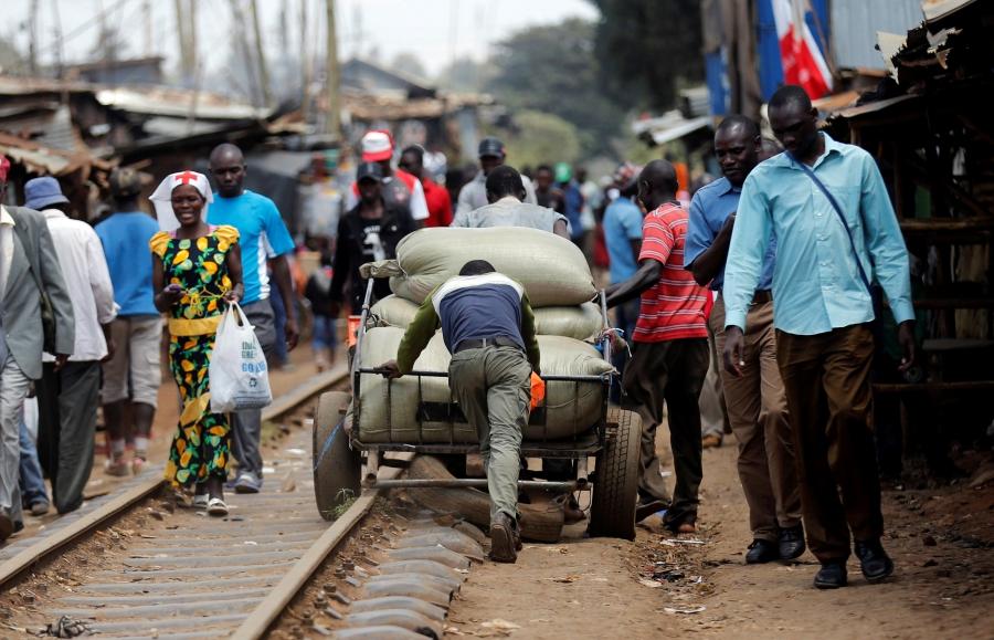 People push a hand cart loaded with maize sacks along the railway line ahead of the presidential election in Kibera slums of Nairobi, Kenya.