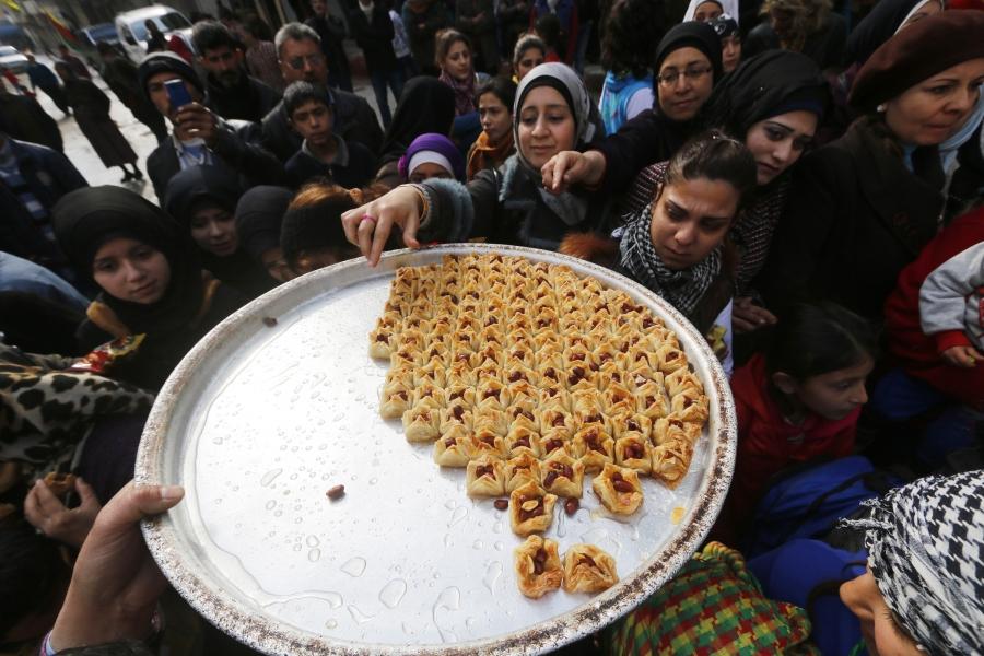 Kurdish civilians offer sweets in celebration after it was reported that Kurdish forces took control of the Syrian town of Kobane, in Sheikh Maksoud neighborhood of Aleppo.