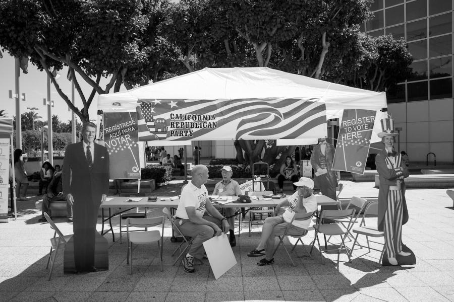 Volunteers sitting in chairs at an otherwise empty booth, large Ronald Reagan cutout on left