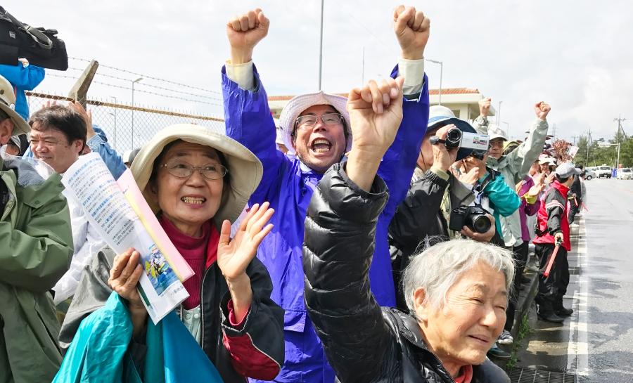 Etsuko Urashima stands left among several oether protesters — arms raised — in Henoko, Japan
