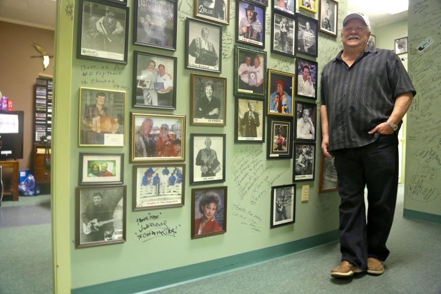Paul Marx, owner of KBON radio station in Eunice, LA, stands near a collection of autographed photos and a wall covered in signatures. His station mostly plays music by Louisiana musicians, including Jamie Bergeron & The Kickin’ Cajuns, whose song “Regist