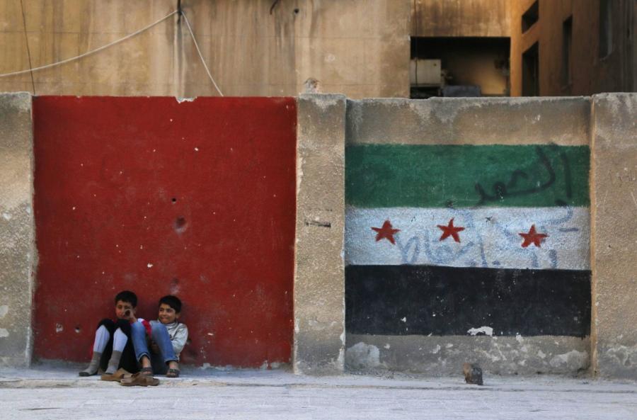 Children sit next to a wall painted with an opposition flag along a street in Aleppo on November 8, 2014. 