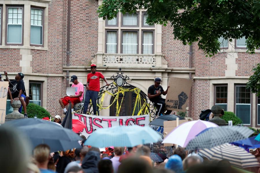 A crowd holds up signs and umbrellas in front of building