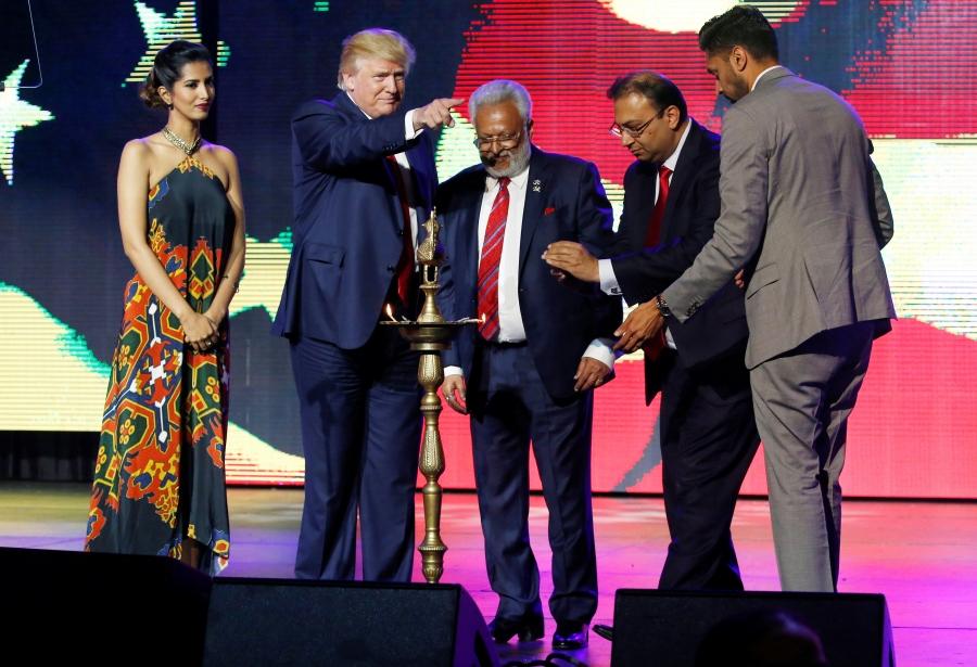 People on stage with Donald Trump, with ceremonial lamp in front.