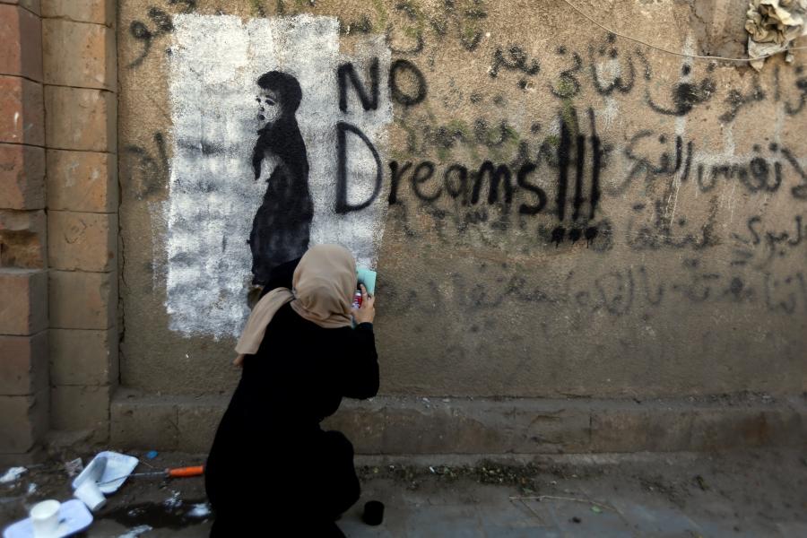 An artist paints graffiti on a wall in Sanaa