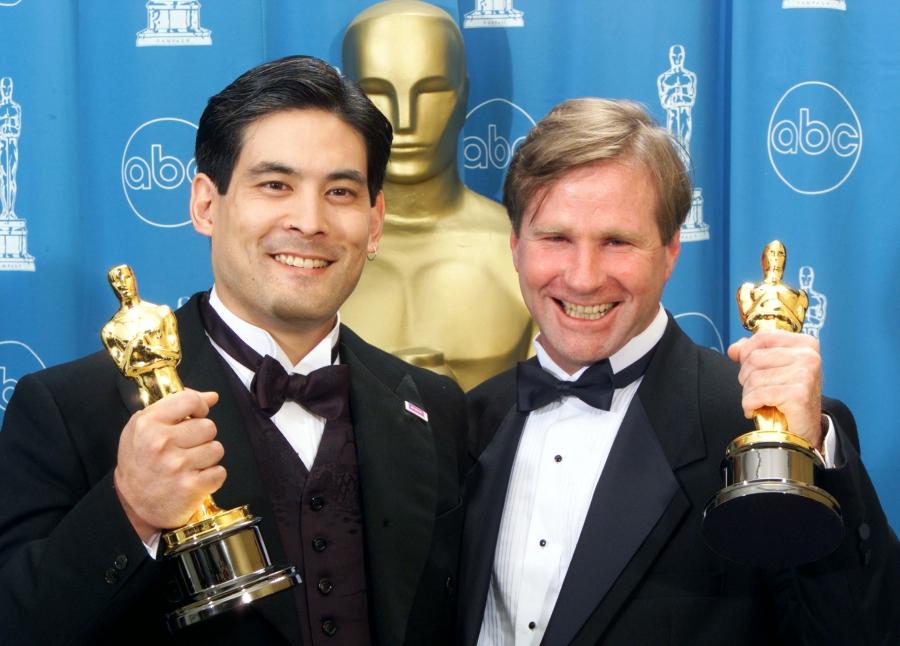 Two men in tuxedos show their Oscars statues to the cameras.