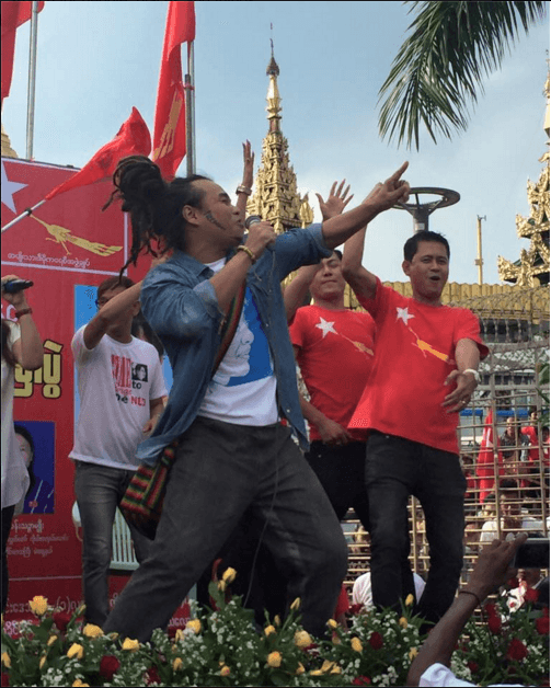 Reggae singer Saw Phoe Khwar sings into the microphone as rapper Anegga (right front) dances along at a performance in downtown Yangon, Oct. 18, 2015.