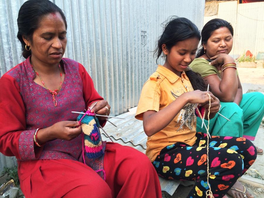 Shreesha Duwal (middle) knits with her mother (left) outside the shack where they now live. They sell the gloves they knit to make extra money. 