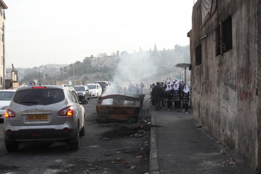 Schoolgirls pass a dumpster filled with burning garbage in Shuafat refugee camp in November 2014. People burn trash because trash collection is haphazard there.