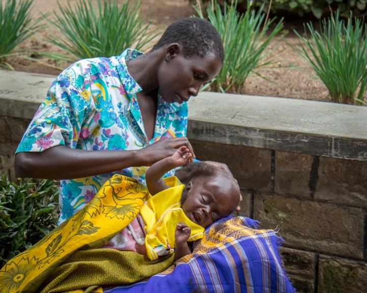 Outside the hospital, a mother shaves her child's head in preparation for neurosurgery.