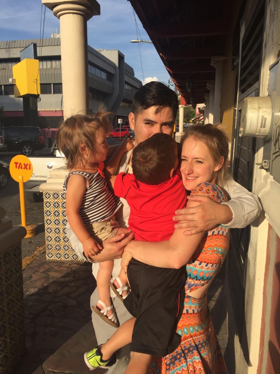 Two adults and two small children hug in circle, standing on sidewalk