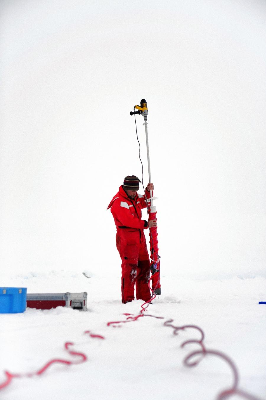 Chris Polashenski uses an electric drill to core out a sample of sea ice. He uses the cores to investigate the tiny cracks in the ice that may or may not allow water to drain from melt ponds
