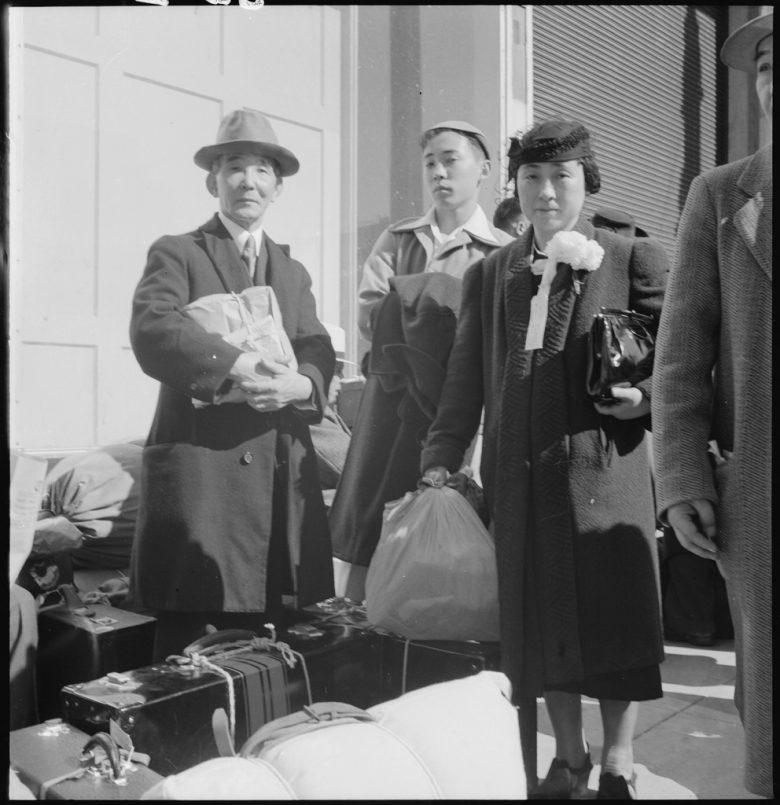 A woman and two men stand with their luggage, in traveling clothes