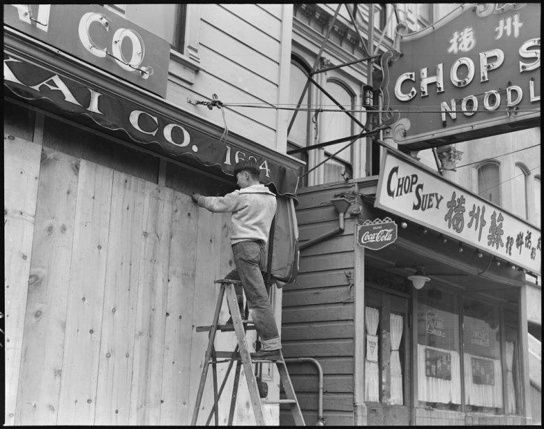 A man on a ladder installs boards on a shopfront