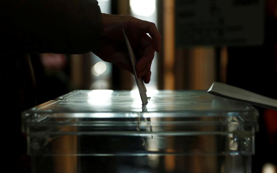 A close-up of a hand dropping a white ballot into a ballot box in Spain.