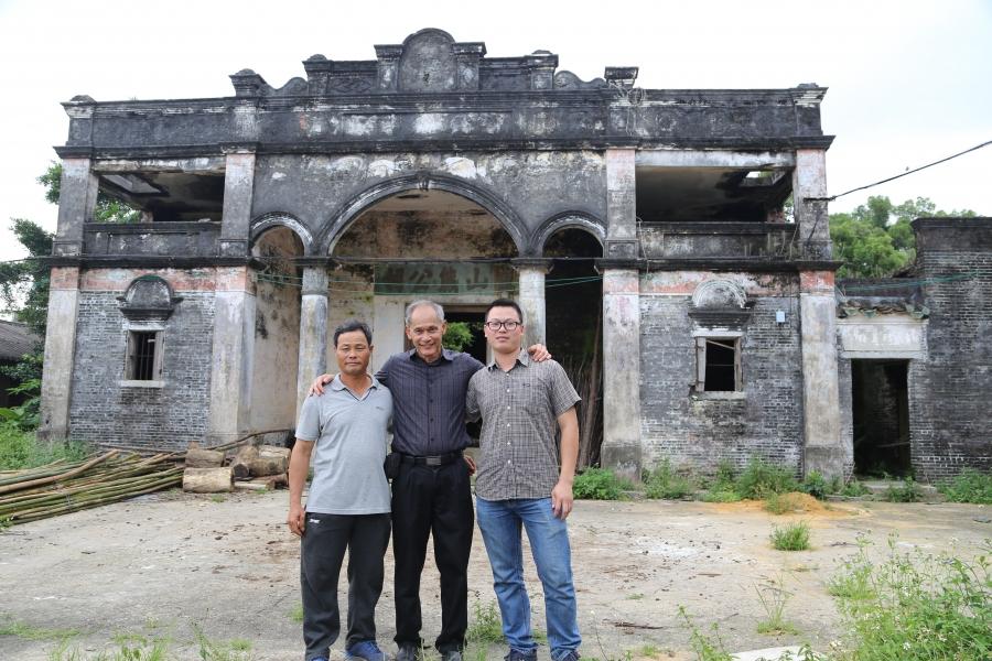 Three men stand in front of an old home.