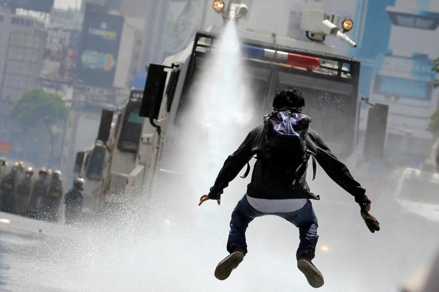 A demonstrator jumps away from a jet of water released from a riot security forces vehicle during a rally against Venezuela's President Nicolas Maduro in Caracas, Venezuela, May 26, 2017.