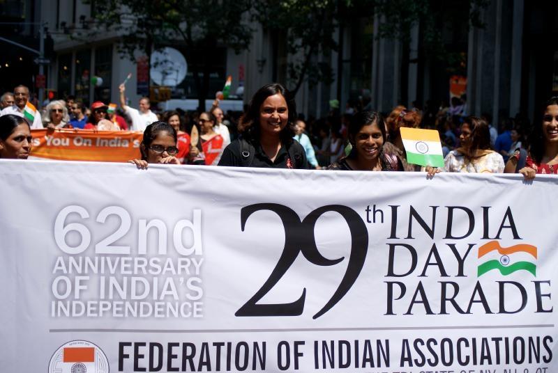 Woman stands in crowd behind sign that reads “29th India Day Parade”