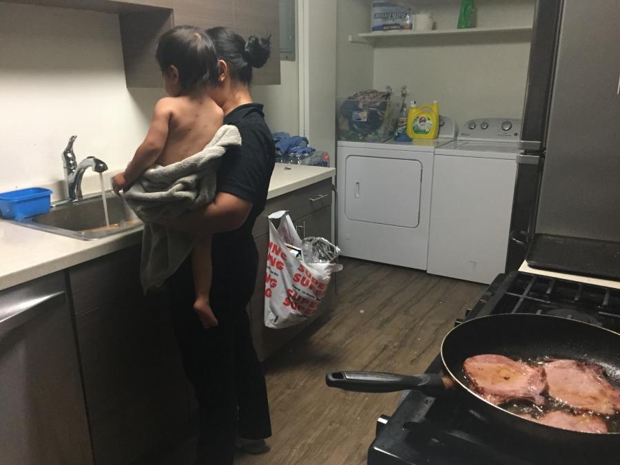 Woman holding toddler who has bumps on his back, in front of stove while she is cooking