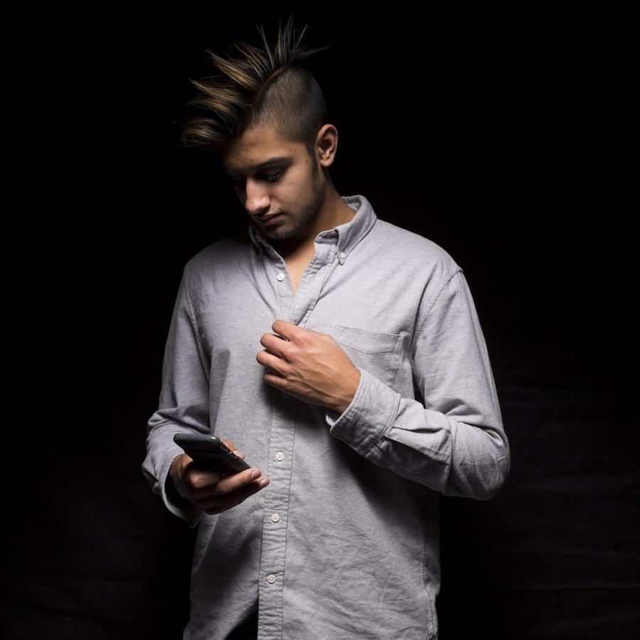 Man with mohawk looking down at phone, against black background