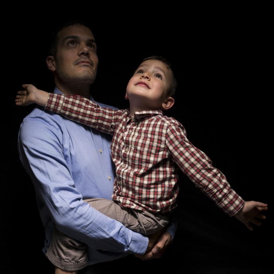 Man holding toddler whose arms are outstretched, against balck background