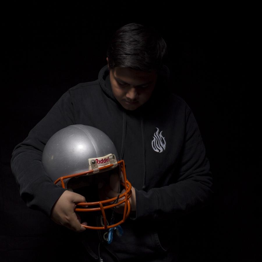 Young man against black bakcground, holding football helmet