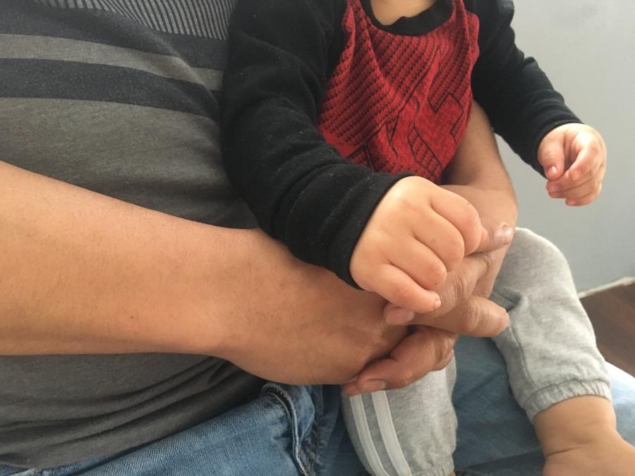 Close up of man's hands with small child on lap, small hands holding larger one