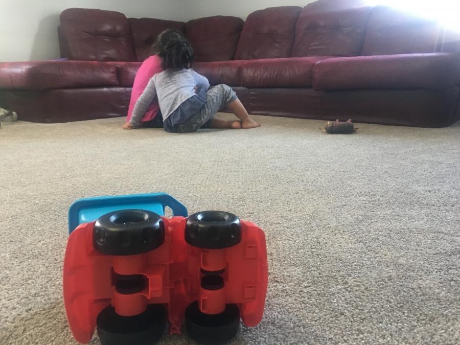 Two girls playing next to sofa with backs to camera, toy truck in the foreground