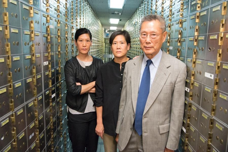Two women and an older man stand in a hallway of deposit boxes.