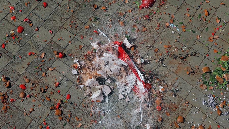 Red shards of clay pot and water are mixed together on the tiled street as the jug hits the pavement and shatters.