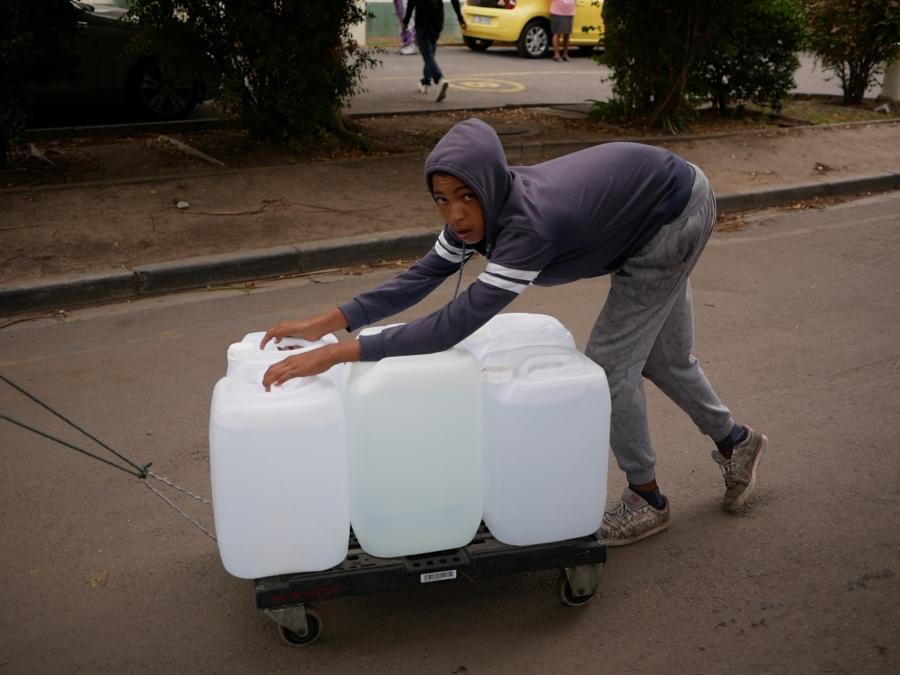 A boy pushes a trolley bulging with white water bottles uphill from the spring. 