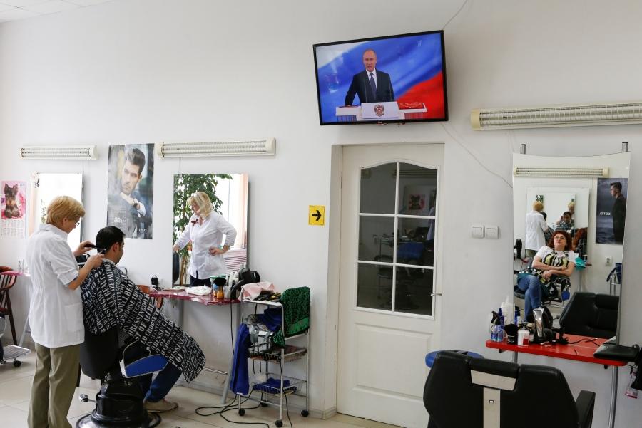 A hairdresser watches Vladimir Putin's inauguration ceremony at a salon in Stavropol, Russia, May 7, 2018.