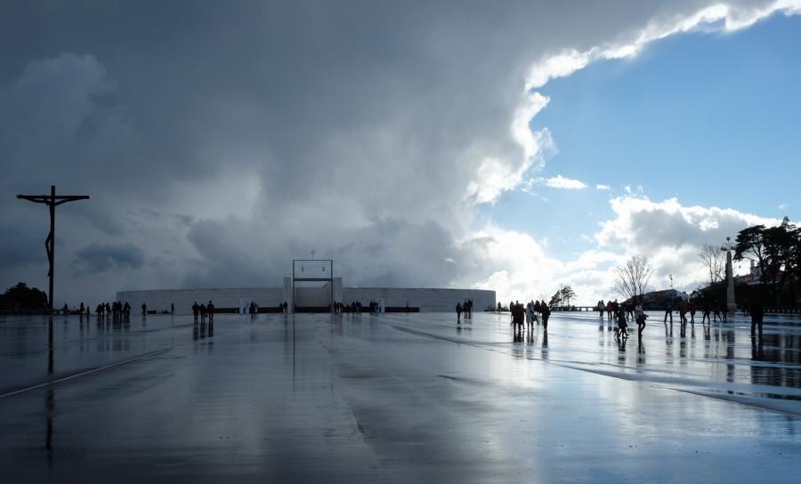 Visitors dot the massive plaza outside the Shrine of Fatima megachurch, under stormy skies