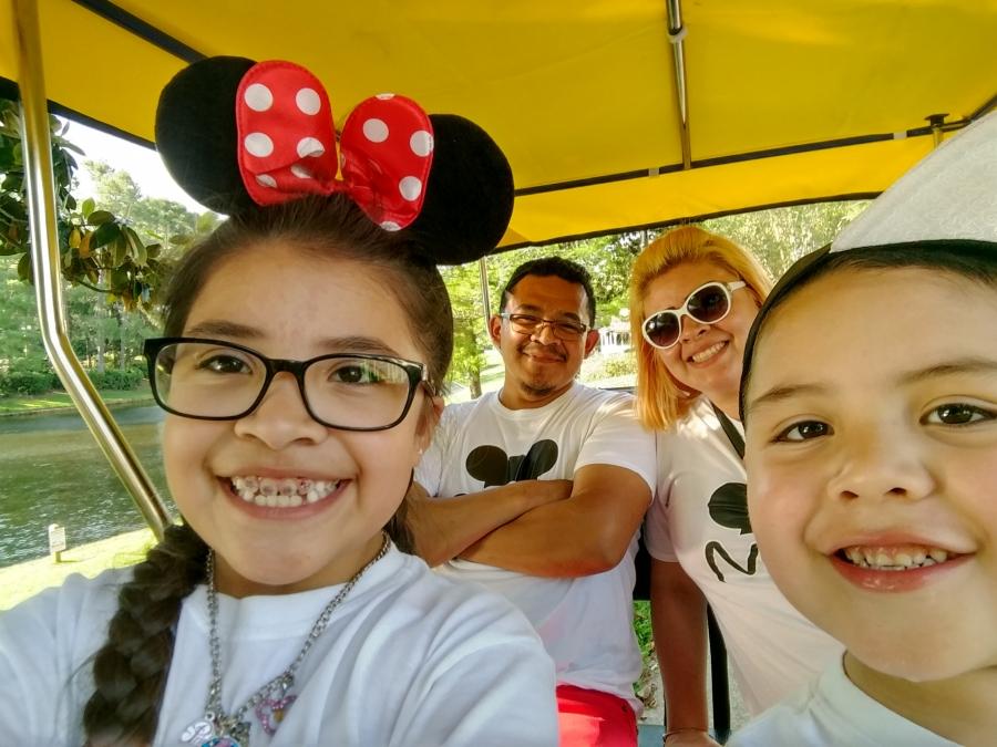 Family in cart, young girl in front with Mickey ears, young boy next to her, parents in back