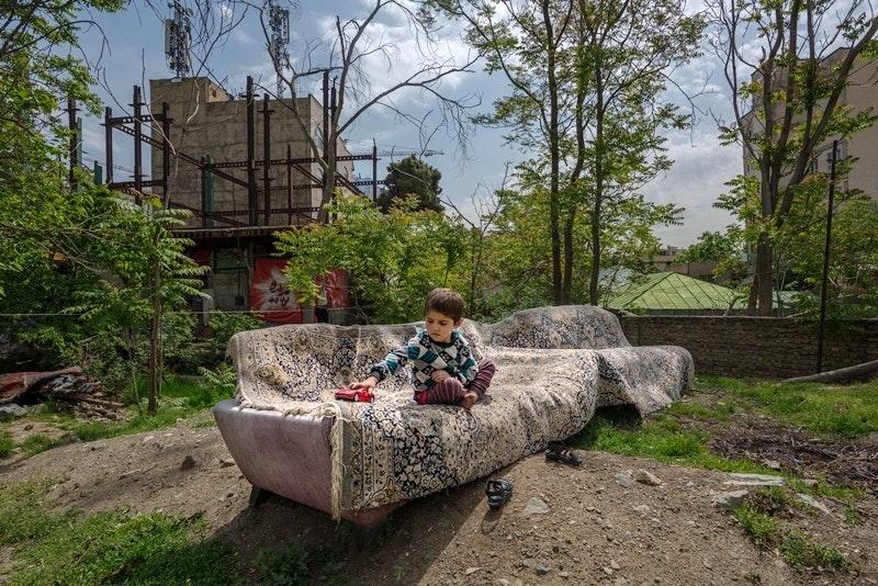A young child sits on a couch outdoors