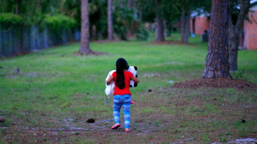 Young girl walking on lawn, holding teddy bears