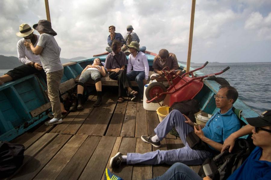 Ten people sit on the wooden deck of small boat.