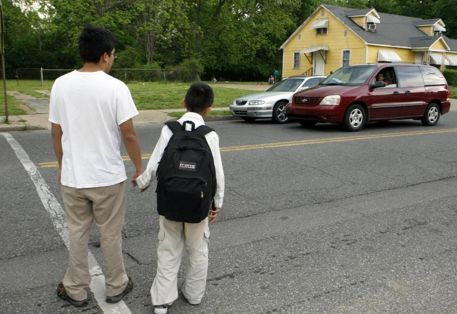 Young man holds hand of boy with backpack, crossing a street